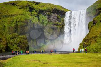 Magnificent famous waterfall Skógafoss, Iceland. A powerful jet Skógar river falls from a large glacier. Tourists delighted the crowd at the foot of roaring jets