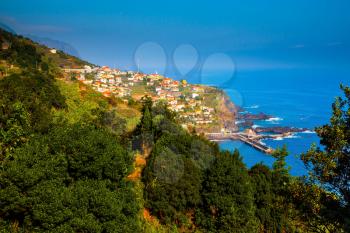 The picturesque village with red roofs on the cape is surrounded by forest. The magical tropical island of Madeira. Concept of exotic and ecological tourism