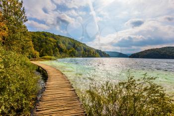 Plitvice Lakes in Croatia on a sunny day. Lush colors of the autumn forest. Wooden flooring for tourists. The concept of ecological and active tourism