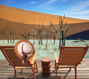 Two wooden folding chairs - deck chairs on a wooden platform. Ecotourism in Namib-Naukluft National Park, Namibia. The bottom of dried lake Deadvlei, with dry trees