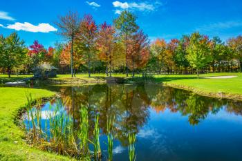  Park of fantastic beauty. Golf Club on the road to Bromont, French Canada. Red, orange and green autumn foliage is reflected to clear water of the lake. Concept of Golf tourism