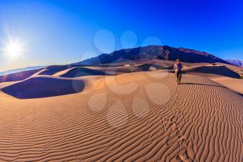 Woman - photographer is among the gently sloping sand dunes. Sunrise in the orange sands of the desert Mesquite Flat, USA
