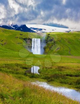 The huge deep falls Skogafoss are reflected in small stream. Grandiose reflection