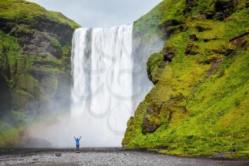 Picturesque huge rainbow appears in the water mist. Middle-aged woman - tourist shocked beauty waterfall. Interesting waterfall in Iceland - Skogafoss