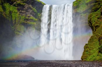 Picturesque rainbow appears in the water mist. The most popular waterfall in Iceland - Skogafoss. Water rushes down with a crash, forming a cloud of mist
