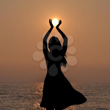 Silhouette of young woman holding the sun in her hands