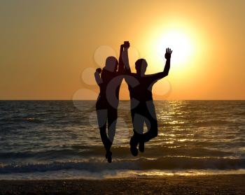 Silhouette of two friends jumping on beach during sunrise time