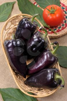 Royalty Free Photo of Black Peppers in a Basket With a Tomato Beside It
