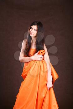 Attractive girl in orange fabric studio shot over brown background