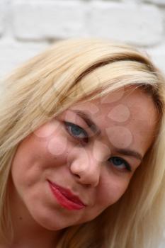 A stunningly beautiful young blond woman with bright blue eyes against wall