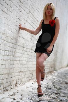 beautiful young girl in black dress with red flower against a brick wall