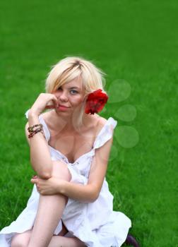 Outdoor portrait of an attractive blond female in a white Spring dress sitting in a forested grassy meadow playing a flute.