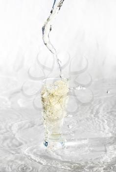 Yelllow drink being poured in a transparent glass with splashes on white