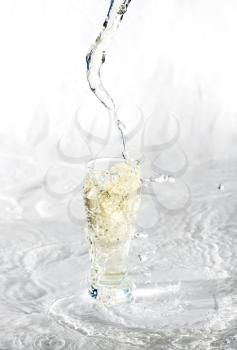 Yelllow drink being poured in a transparent glass with splashes on white