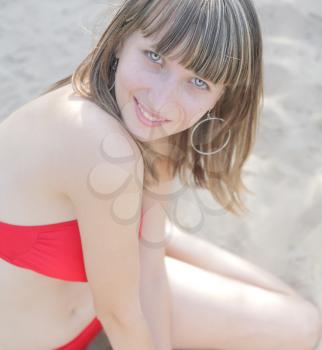 Beautiful girl sitting on the sand red bikini