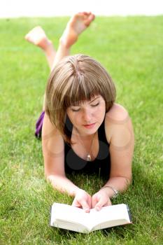 Young beautiful girl reading in the park laying on the grass