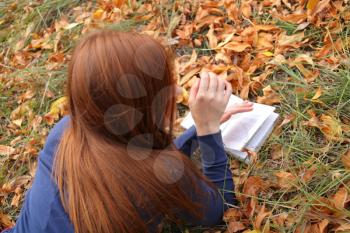 Redhead woman lies on green grass and reads book, Happy smiling beautiful young university student studying lying down in grass.