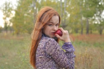 Beautiful young redhead in a autumn meadow with red apple