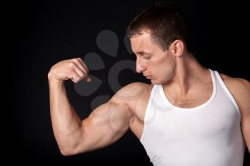 a male in white tank top with strong muscles on the black background