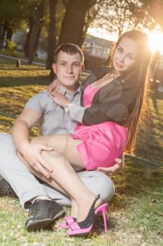 Romantic young couple relaxing outdoors in park on grass in backlit vertical shot