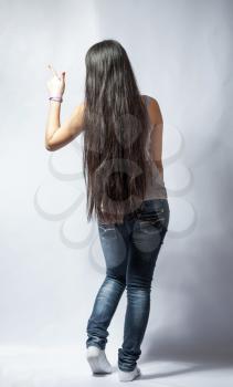 back view of standing young beautiful Asian woman in tank top and jeans. Teen watching. Rear view. Backside view of person. Shot over white background.