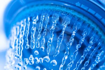 Photograph of a shower head showing drops and streams of water. Blue toned. Shower and flying water drops.