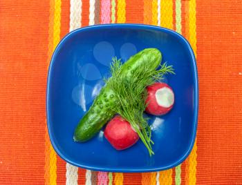 Radish, cucumber in blue bowl on red table cloth