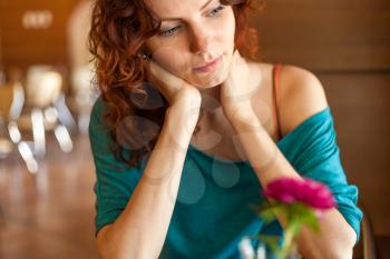 Redhead women sitting in the cafee with pink flower on the table befor and looking at camera and smiling