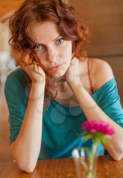 Redhead women sitting in the cafee with pink flower on the table befor and looking at camera and smiling