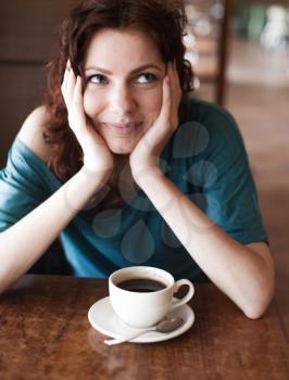 Redhead women sitting in the cafee with cup of coffee on the table befor and looking at camera