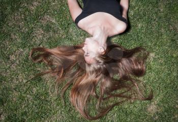 Smiling woman laying on grass. Beautiful young girl is lying on green grass in the evening time. The girl lays on a grass of a meadow.