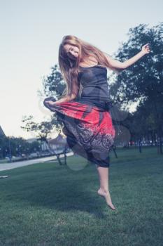 Dancing in park. Alone and happy. Long haired women make jump outdoors at evening. Vertical shot. Toned image