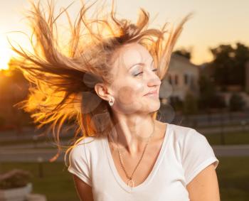 blonde female with hair flying in the  wind on sunset backlit