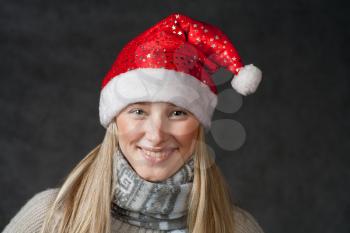 Front view of the smiling blond female in Santa hat. Pretty blond wearing christmas hat on dark background