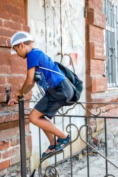 Child boy climbing over metal fence in a street, side view.