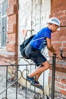 Child boy climbing over metal fence in a street, side view.