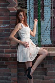 Young women in white dress standing hear red brick fence and posing in fashion style