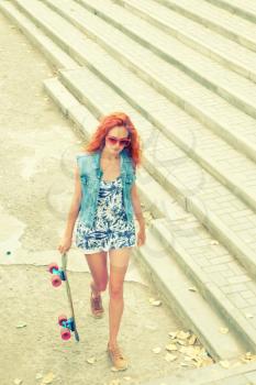 Portrait of a pretty girl with a skateboard in her hand and sunglasses, outdoors, from above view