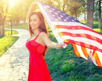 Cute female in red dress with American nation flag in her hands. Happy young woman holding american flag