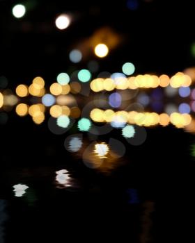 Yellow and green spots on black. Blurred city at night, bokeh background. Reflection of colorful lights in water and a lot of copyspace
