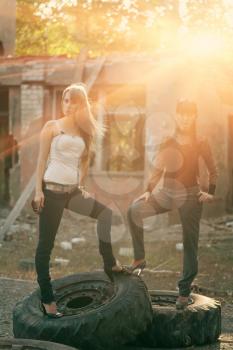Full body shot of a two women standing on a tyres outdoors backlit