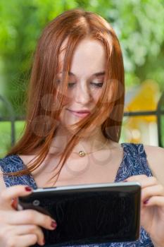 Redhead student leaning against a tree using her tablet on college campus. Redhead woman with tablet outdoors
