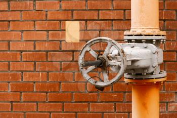 Gas valve on yellow natural gas distribution industrial pipe in front of red brick wall with copyspace vintage color-look
