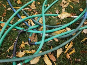Garden hose, watering equipment are lying on grass covered with fallen leaves