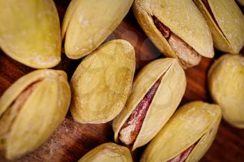 Salted pistachio nuts macro image. A lot of salty pistachios lies on a wooden background with open shells