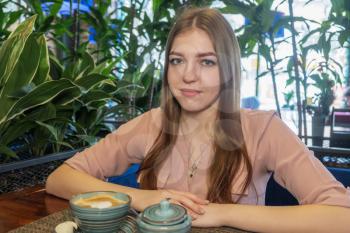 Nice blond haired girl with cup of cappuccino in fashionable cafeteria