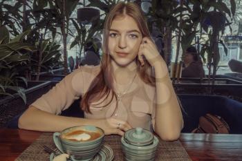 Sad lovesick lady is posin sitting in cafe. there are coffee cup and sugar bowl in front of her. She is touching her head by hand. Front view. Frustration.