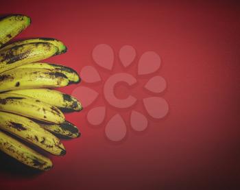 Retro styled image of Organic bananas on red background top view. Bunch of bananas is lying on orange background with dark spots marking ripening process.
