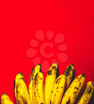 Many bananas on red background with copyspace top view. Bunch of bananas is lying on orange background with dark spots marking ripening process.