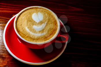 Red coffee cup with froth art on top foam served on wooden table, above view, copyspace on right